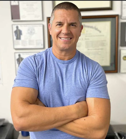 Dr. Rob Jones smiling in a blue t-shirt with diplomas in the background